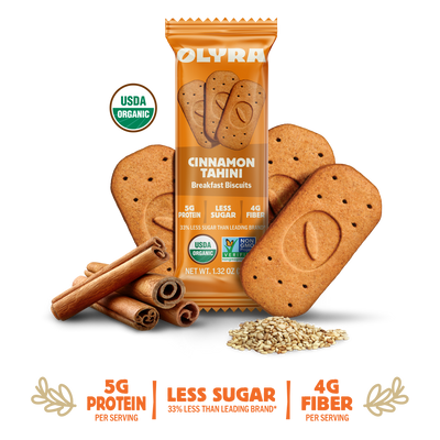 Olyra Cinnamon Tahini breakfast biscuits with packaging, cinnamon sticks, and seeds on a white background.