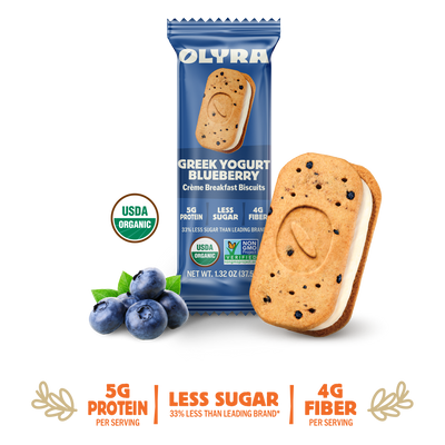 Olyra Greek Yogurt Blueberry cookie with packaging and blueberries on a white background