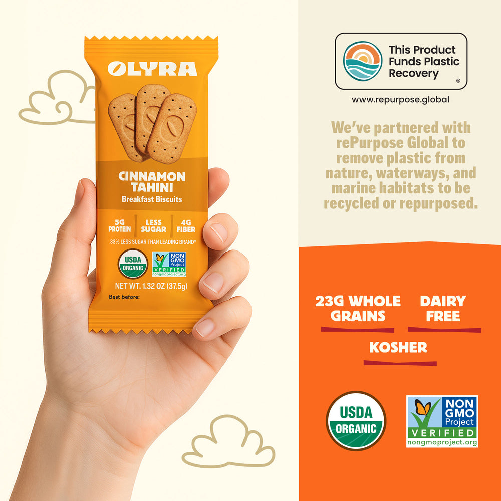 Hand holding a package of Olyra Cinnamon Tahini breakfast biscuits with product details and sustainability information.