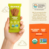Hand holding a green Olyra hazelnut carob breakfast biscuit package with product details on an orange background.