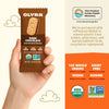 Olyra dark chocolate crème breakfast biscuits packaging held by a hand, with product details and sustainability information on an orange background.