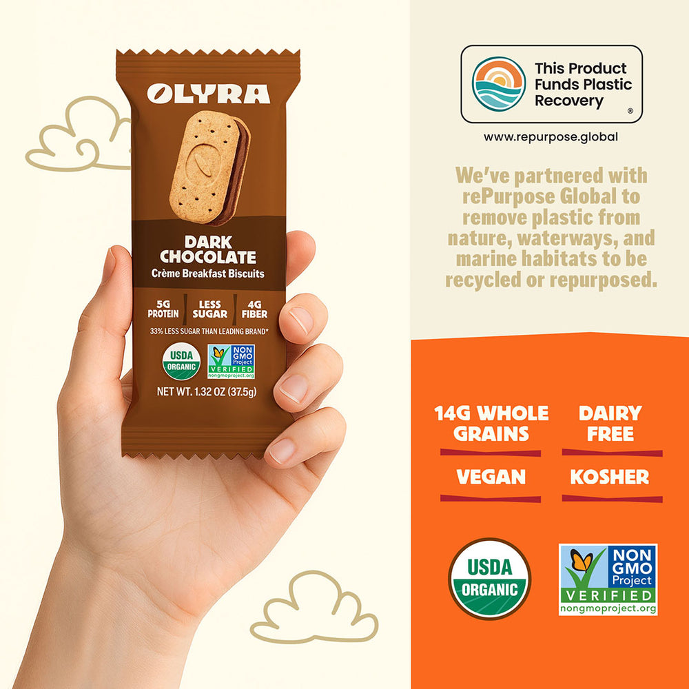 Olyra dark chocolate crème breakfast biscuits packaging held by a hand, with product details and sustainability information on an orange background.