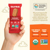 Hand holding a red Olyra hazelnut breakfast biscuit package with product details on an orange background.