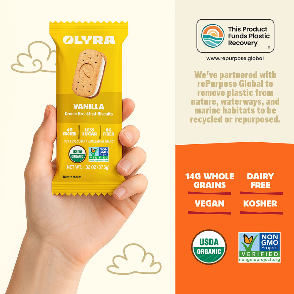 Hand holding a yellow Olyra vanilla crème breakfast cookies package with product details on an orange background.