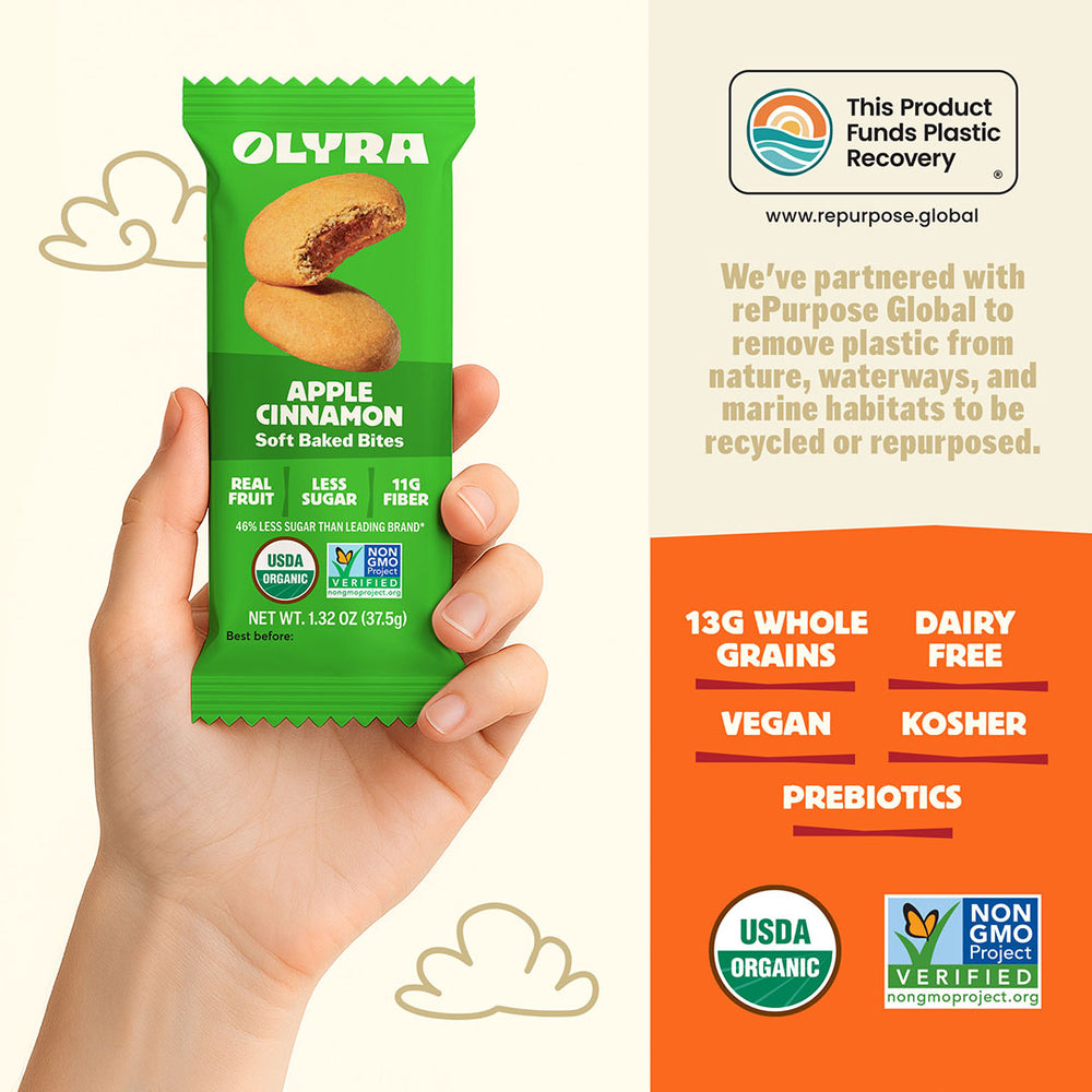 Olyra Apple Cinnamon soft baked bites packaging held in a hand with product details on an orange background.