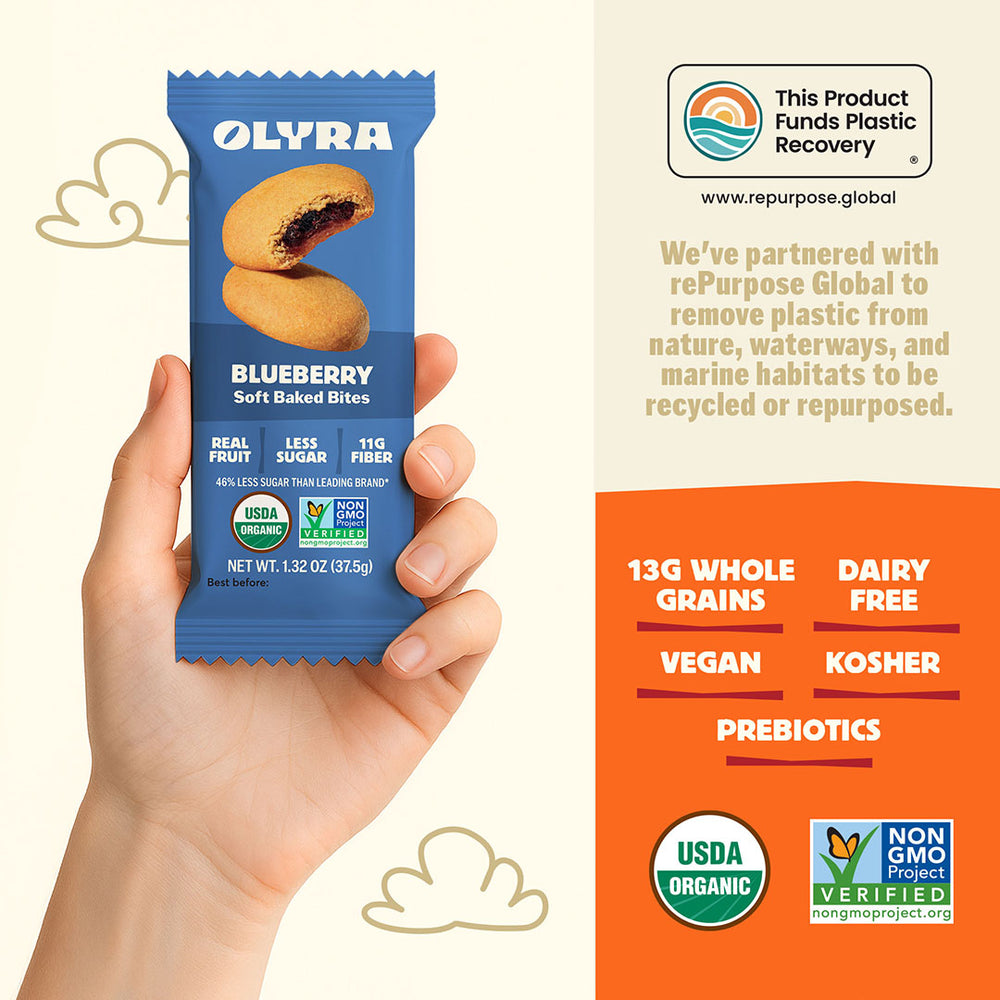 Olyra blueberry soft baked bites package held by a hand with product details on an orange background.