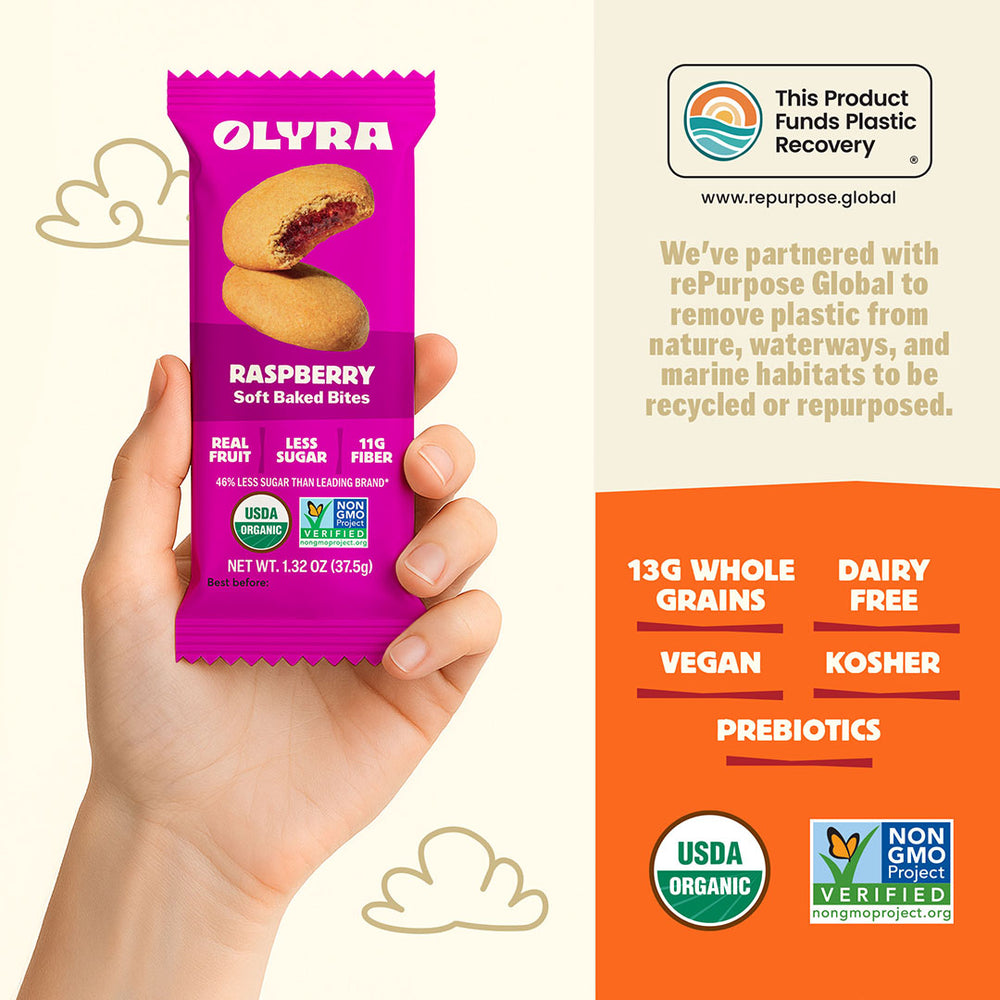 Purple Olyra raspberry soft baked bites package held by a hand with product details on an orange background.