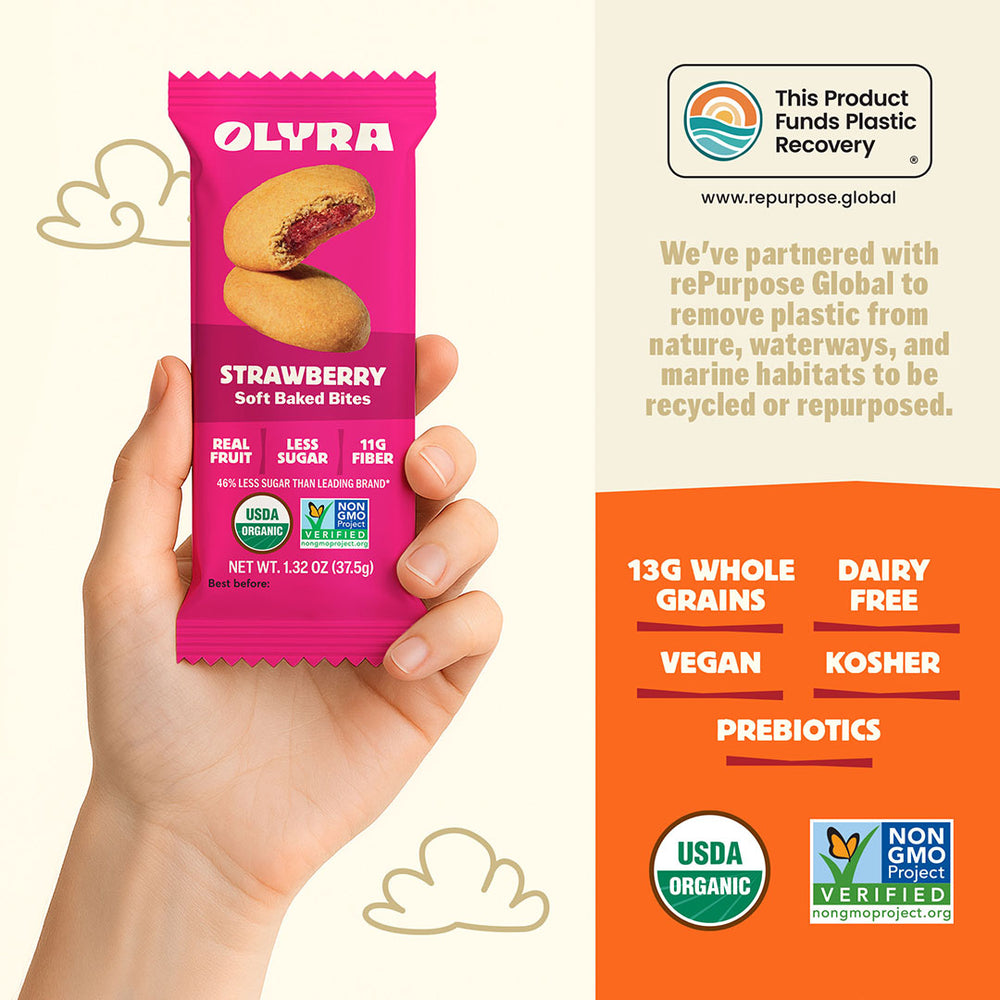 Olyra strawberry soft baked bites packaging held by a hand with product details on an orange background.