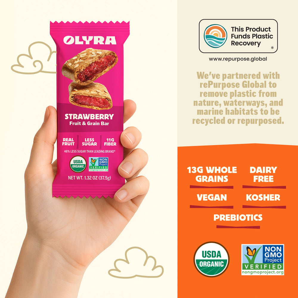 Olyra strawberry fruit and grain bar packaging held by a hand, with product details and certification logos on an orange background.