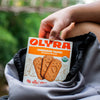 Person grabbing a box of Olyra Cinnamon Tahini breakfast biscuits out of a backpack.