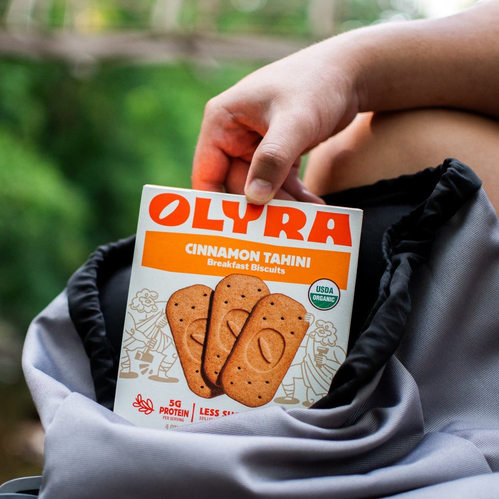 Person grabbing a box of Olyra Cinnamon Tahini breakfast biscuits out of a backpack.