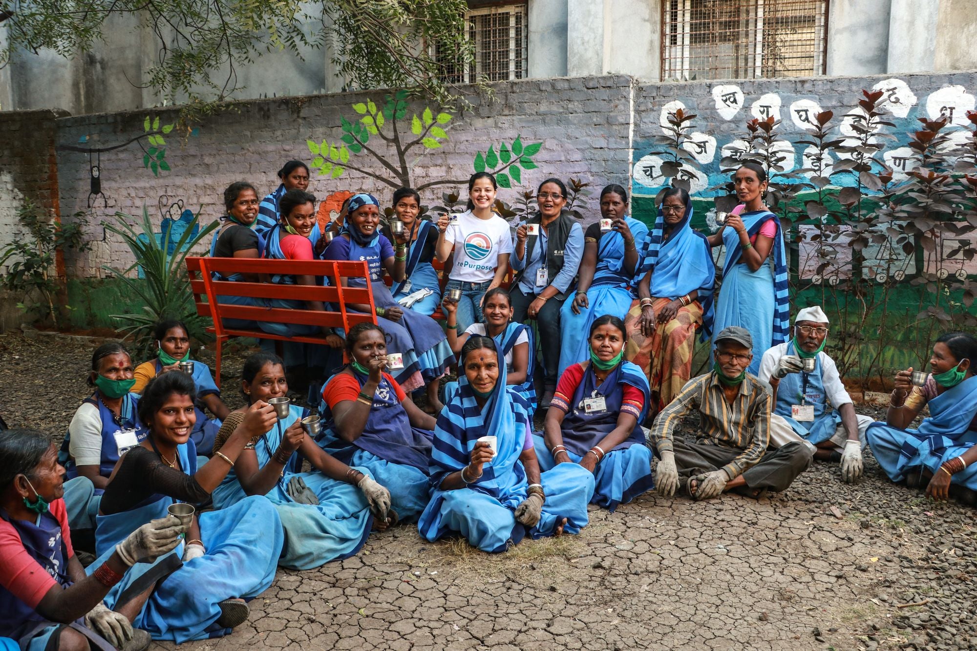 Group of people, including women in blue uniforms, posing in front of a mural.
