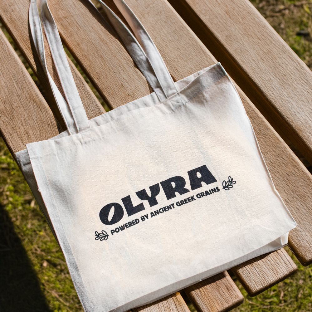 White tote bag with 'OLYRA' branding on a wooden surface